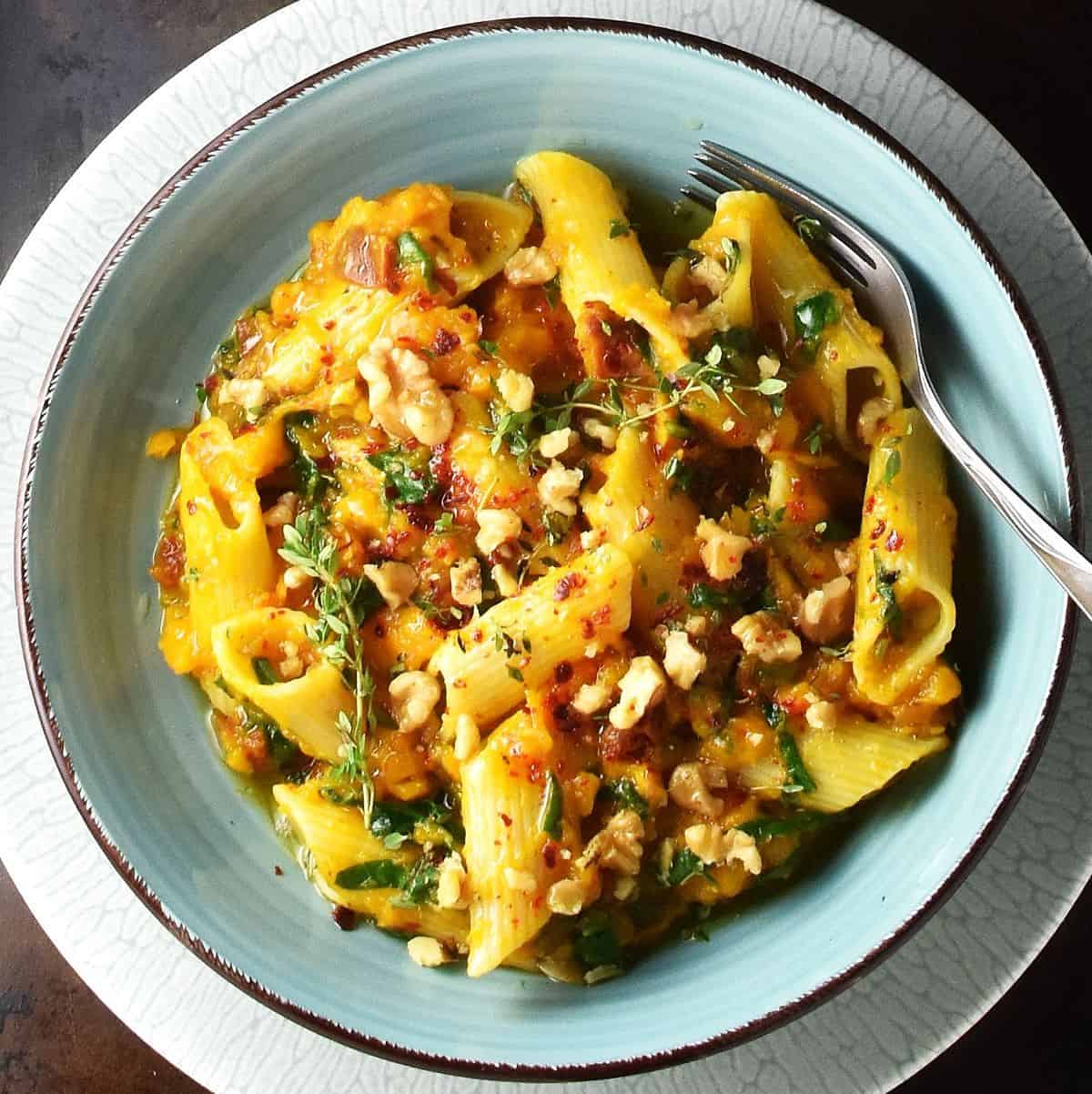 Top down view of roasted pumpkin pasta in blue bowl with fork.