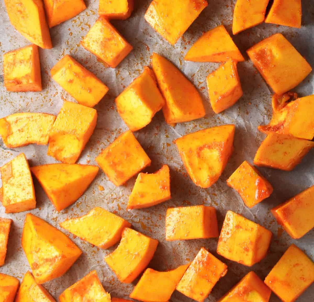Seasoned chunks of peeled pumpkin on parchment.