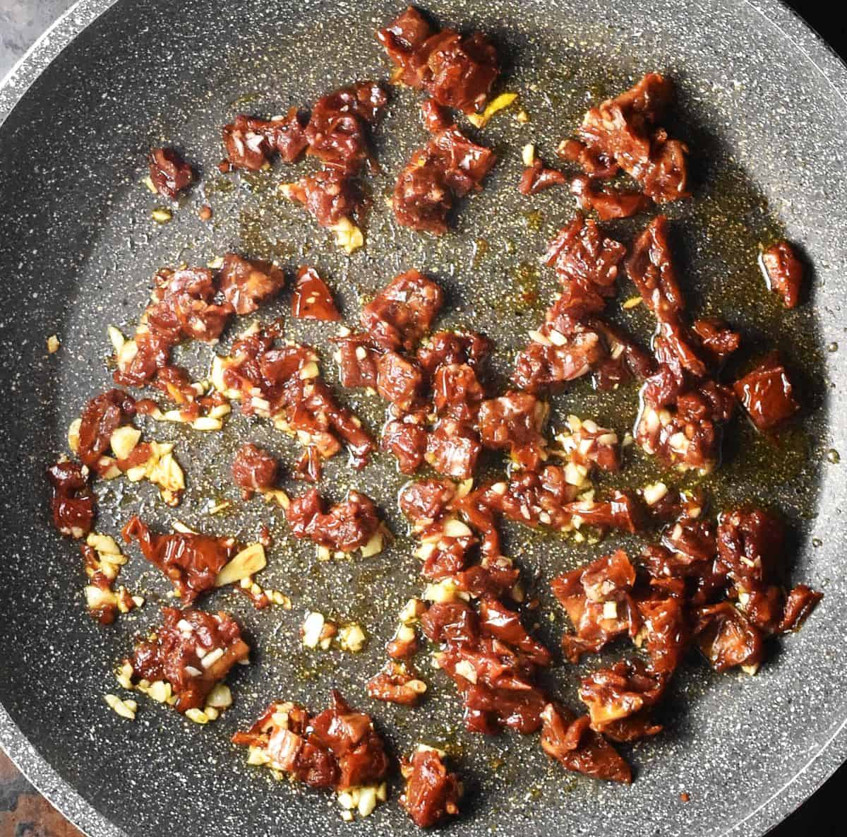 Chopped sundried tomatoes and garlic in large, grey pan.