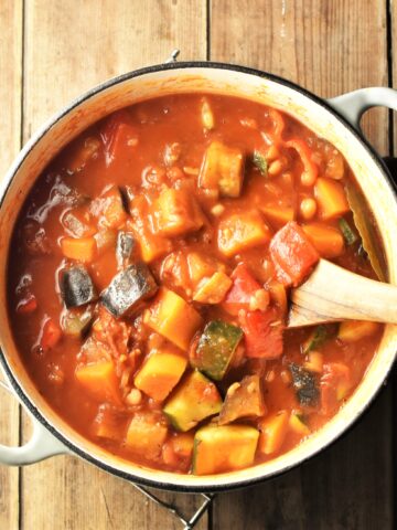 Chunky vegetable stew in tomato sauce in large white post with wooden spoon.