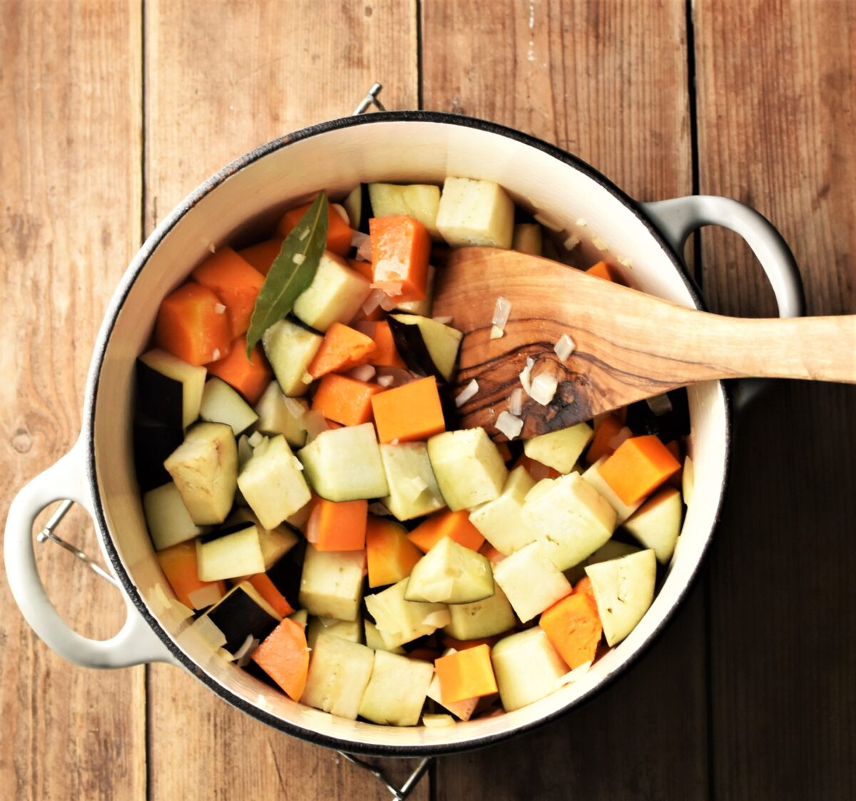 Cubed squash and eggplant in large white pot with wooden spoon.