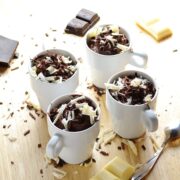 Cheesecake pots with white and dark chocolate shavings, chocolate pieces and spoon on wooden surface.