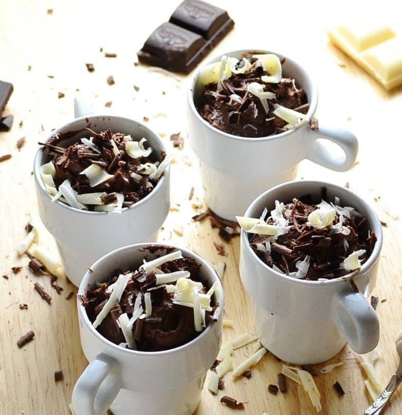 Close-up view of chocolate cheesecake white pots with white and dark chocolate shavings and chocolate pieces on wooden table.