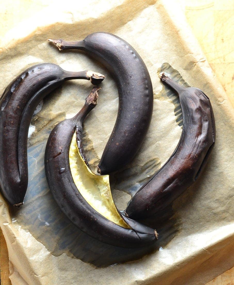 Top down view of 4 dark brown baked bananas on tray lined with baking paper.