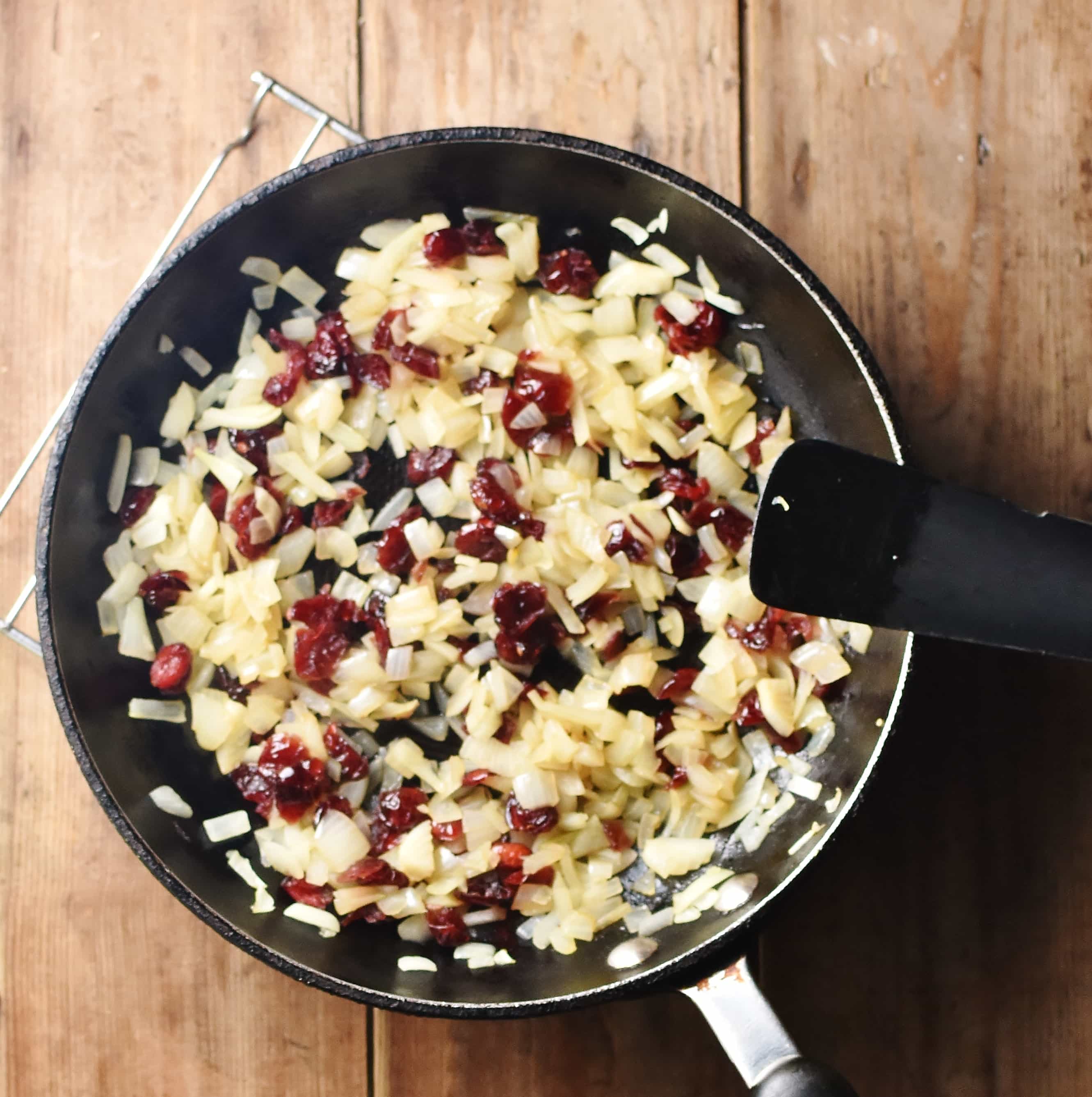 Chopped onions and cranberries in pan with black spatula.