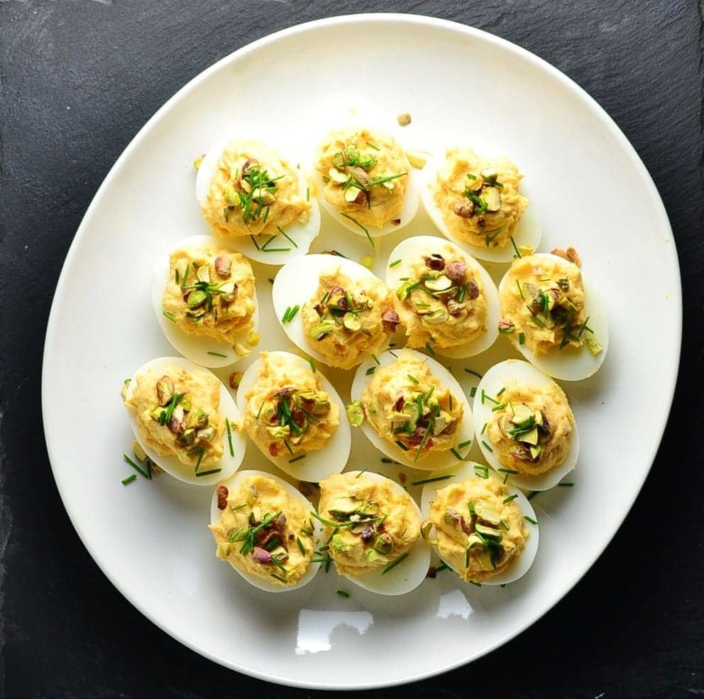 Top down view of smoked salmon deviled eggs with garnish of pistachios and chives on white plate.