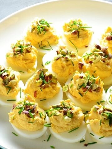 Smoked salmon deviled eggs with garnish of pistachios and chives on white plate.