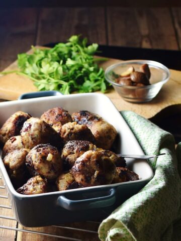 Stuffing meatballs in square blue dish with green cloth to the right, herbs and chestnuts in small dish in background.