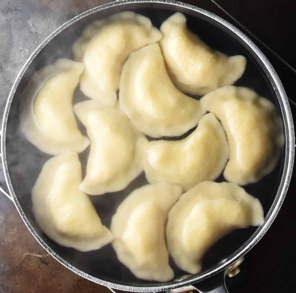 Pierogi floating on surface of pot of water.