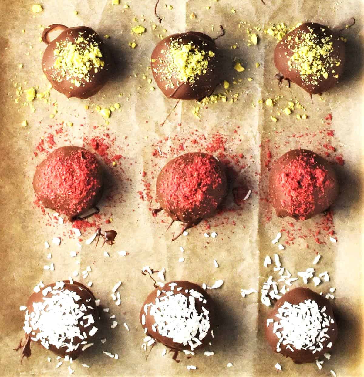Top down view of chestnut chocolate truffles topped with nuts and coconut flakes on parchment.