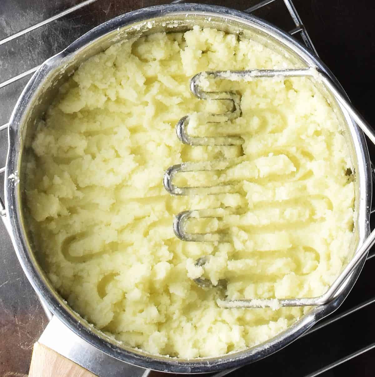 Creamy mashed potato in pot with potato masher.