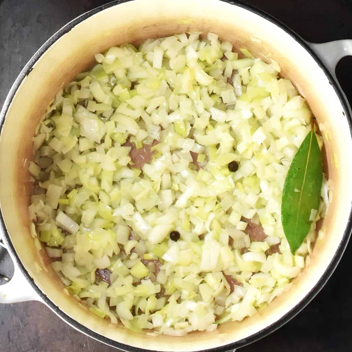 Top down view of sauteed chopped onion with bay leaf in large white pot.