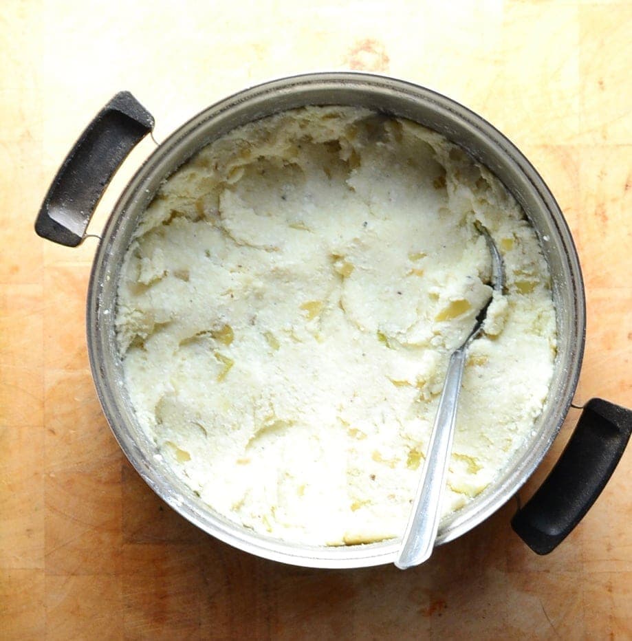 Top down view of Polish cheese and potato pierogi filling in saucepan with spoon on top of wooden surface.