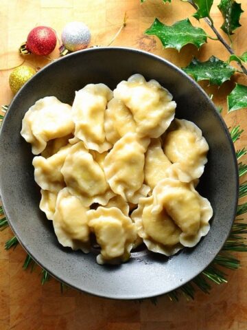Top down view of Polish pierogi in black bowl on top of wooden table with Christmas decorations.
