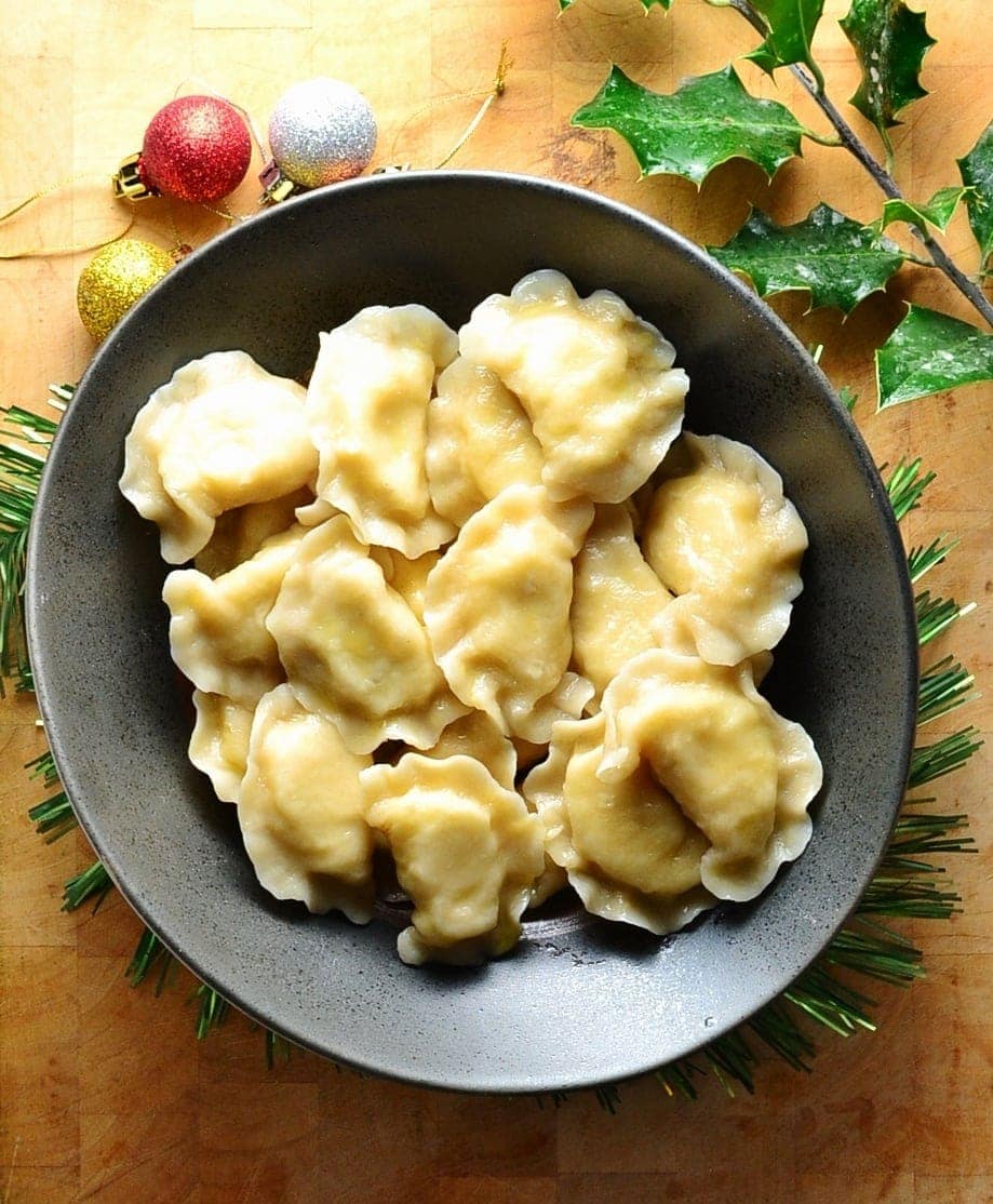 Top down view of Polish pierogi in black bowl on top of wooden table with Christmas decorations.