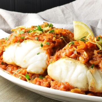 Close-up side view of Polish fish topped with stewed vegetables on white plate.