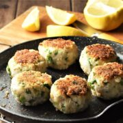 6 fish cakes in pan with lemon in background.