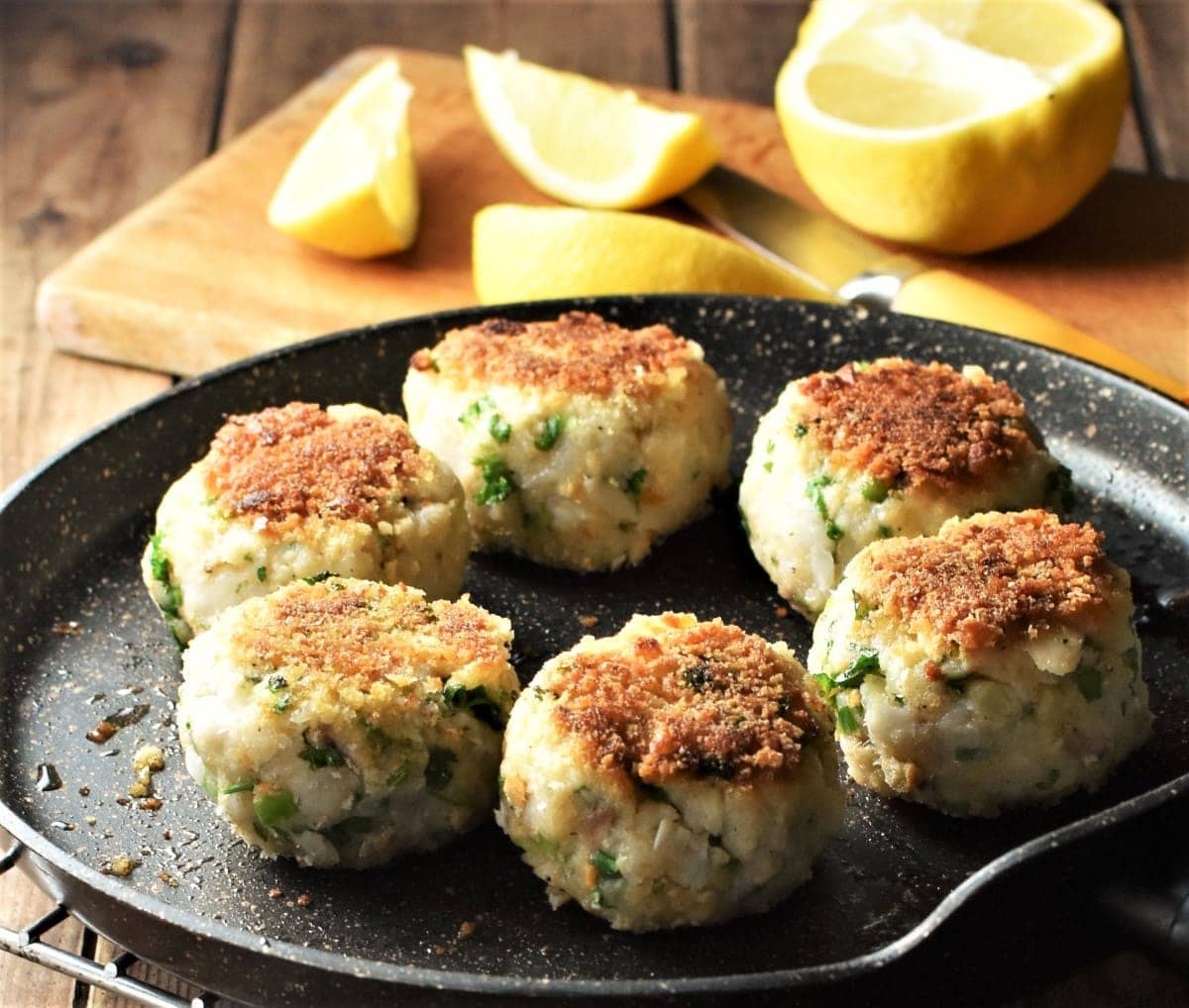 6 fish cakes in pan with lemon in background.