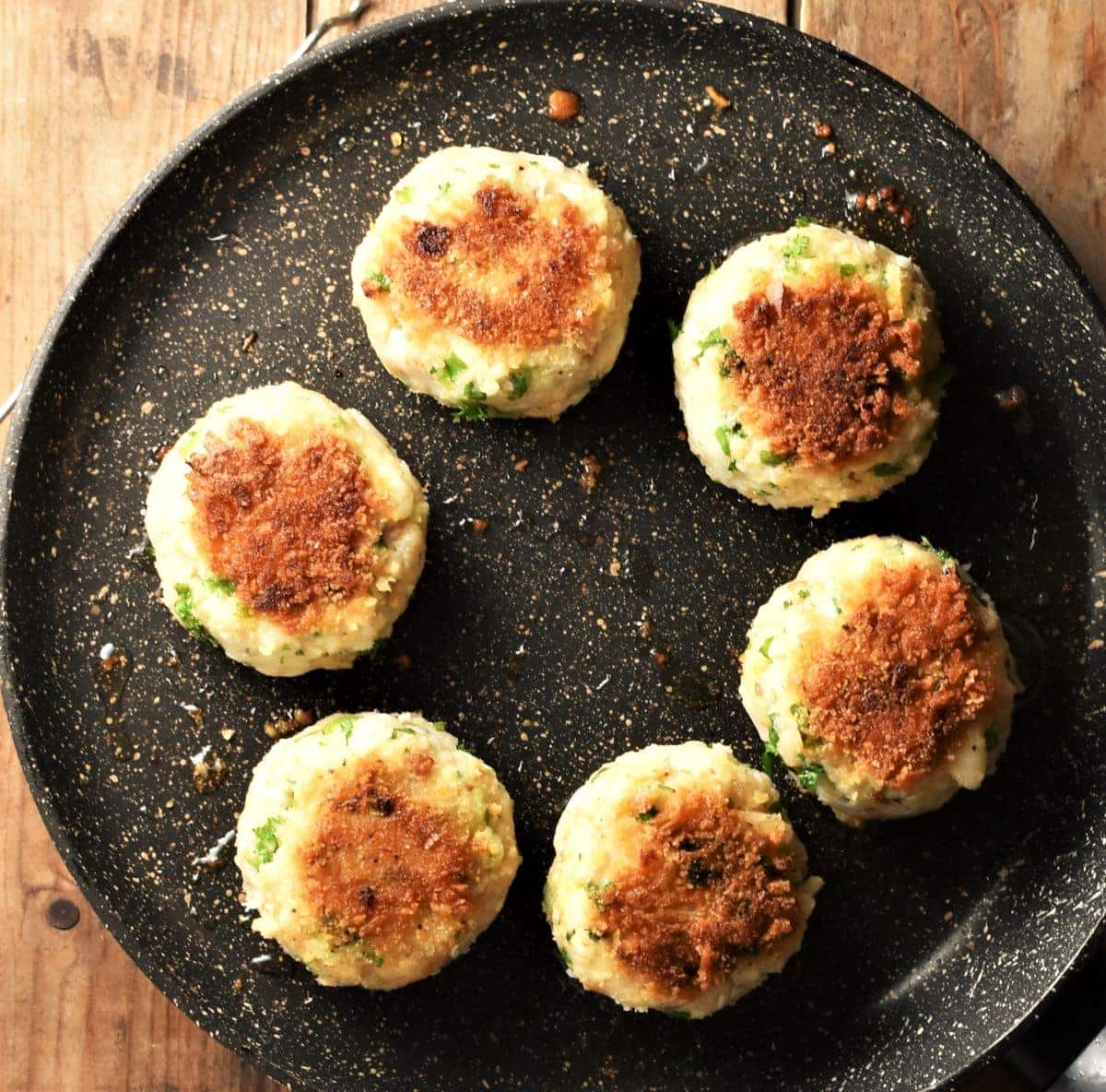 Top down view of 6 fried fishcakes in pan.