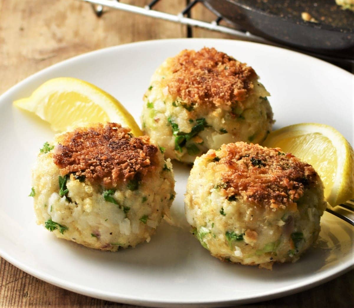 3 breaded fishcakes on top of plate with lemon wedges.