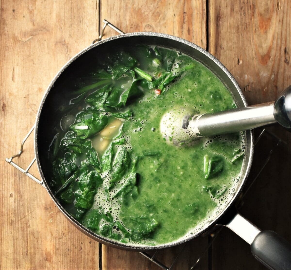 Partly pureed spinach soup in large pot with stick blender end piece.