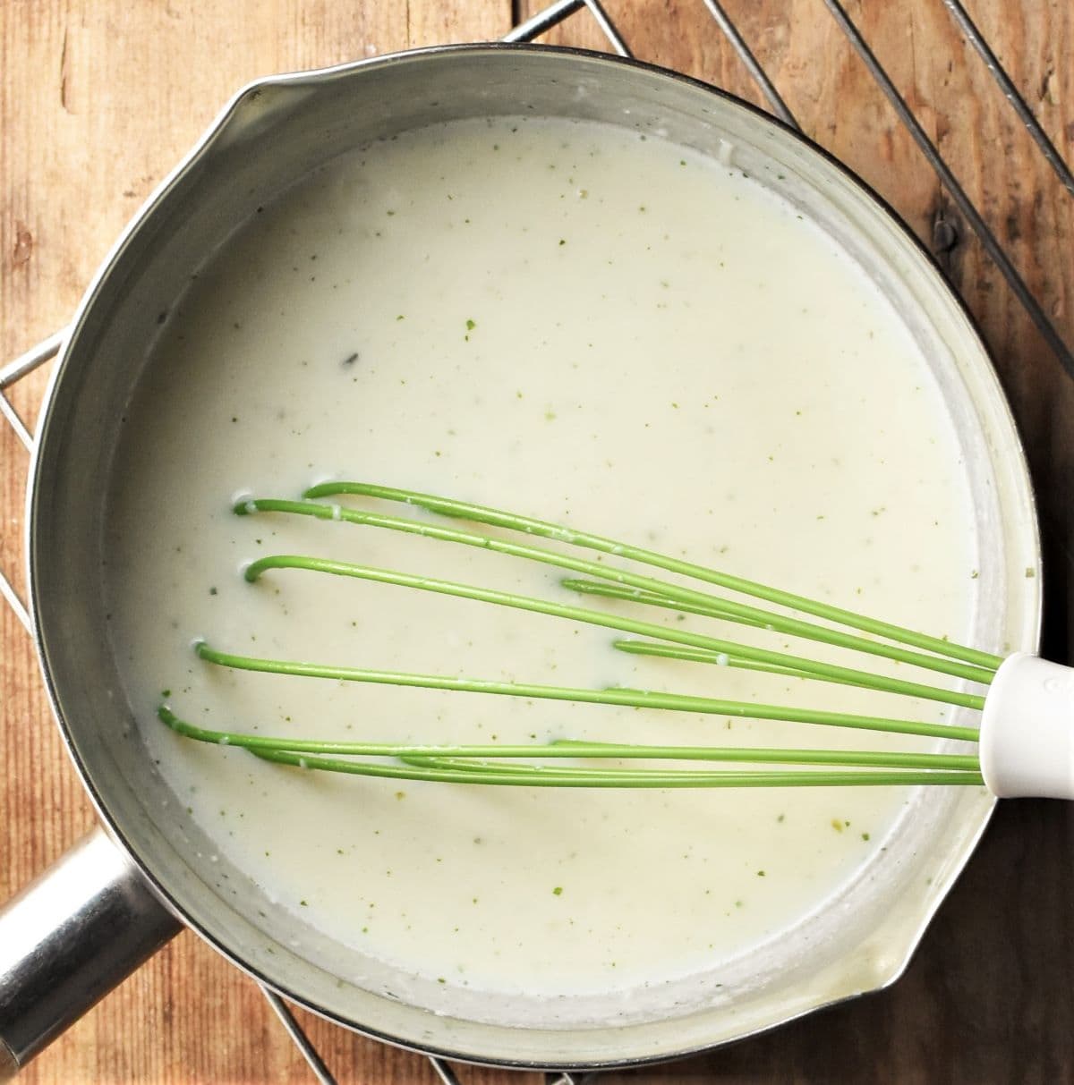 Making creamy sauce for chicken pasta bake in pan with green whisk.