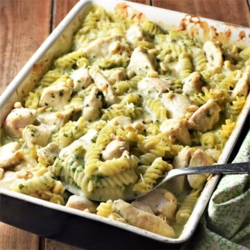 Side view of creamy pesto chicken pasta bake in rectangular dish with spoon.