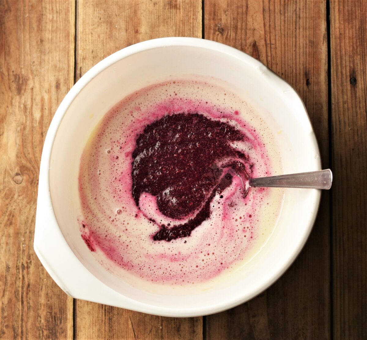 Creamy egg mixture and beet puree in large white bowl with spoon.