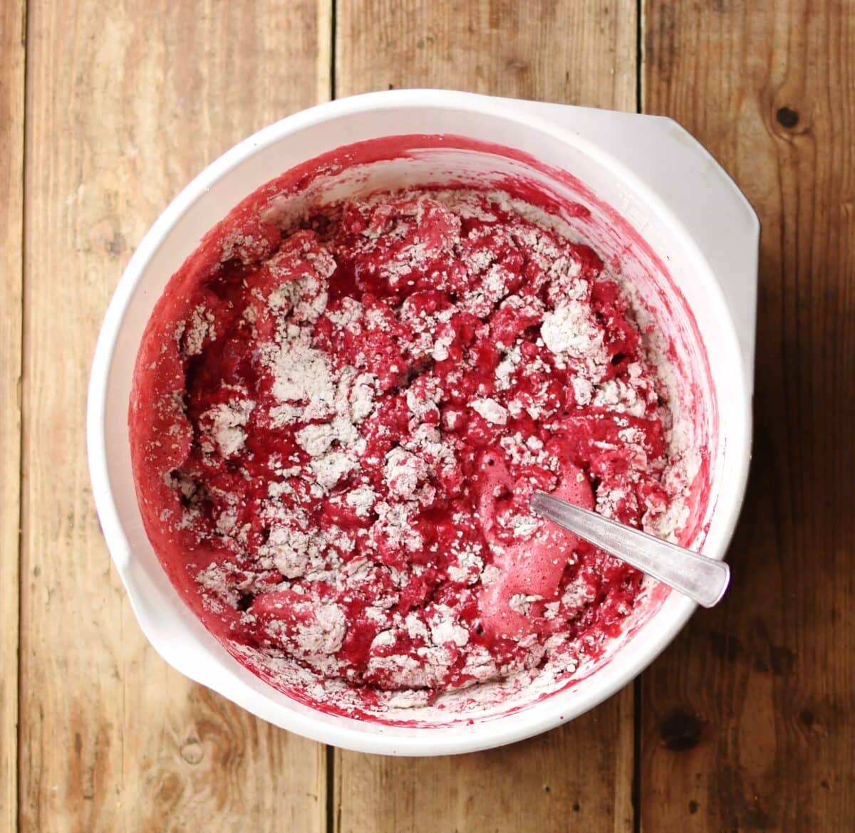 Beetroot bread batter with dry ingredients visible inside white bowl with spoon.