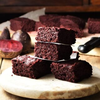 Side view of beetroot brownies on top of round marble plate, with raw beets and brownies in background.