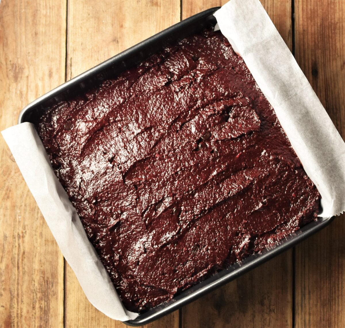 Beet brownie batter in square pan lined with parchment paper.