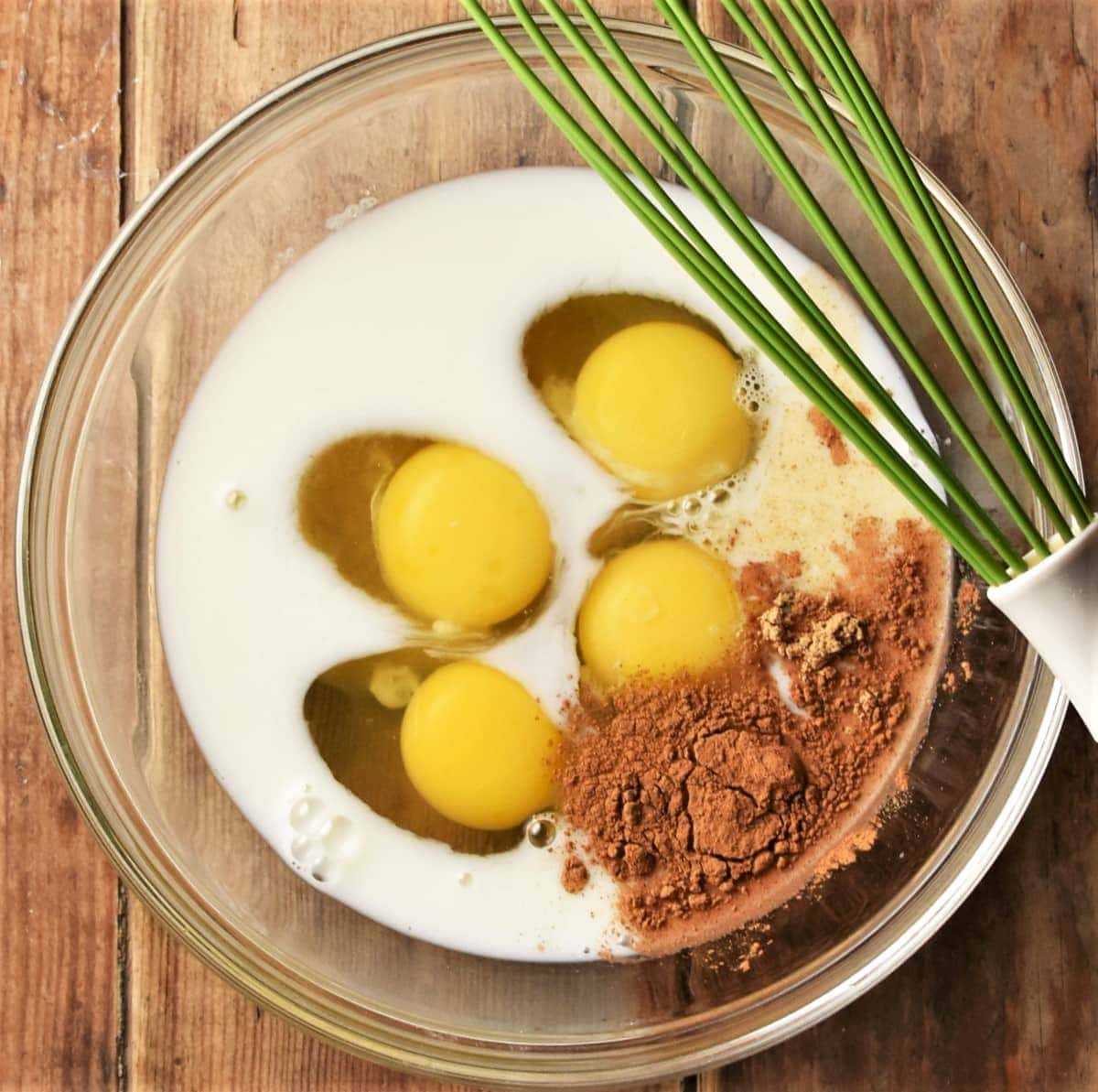 4 eggs with milk and spice in mixing bowl with green whisk on top.