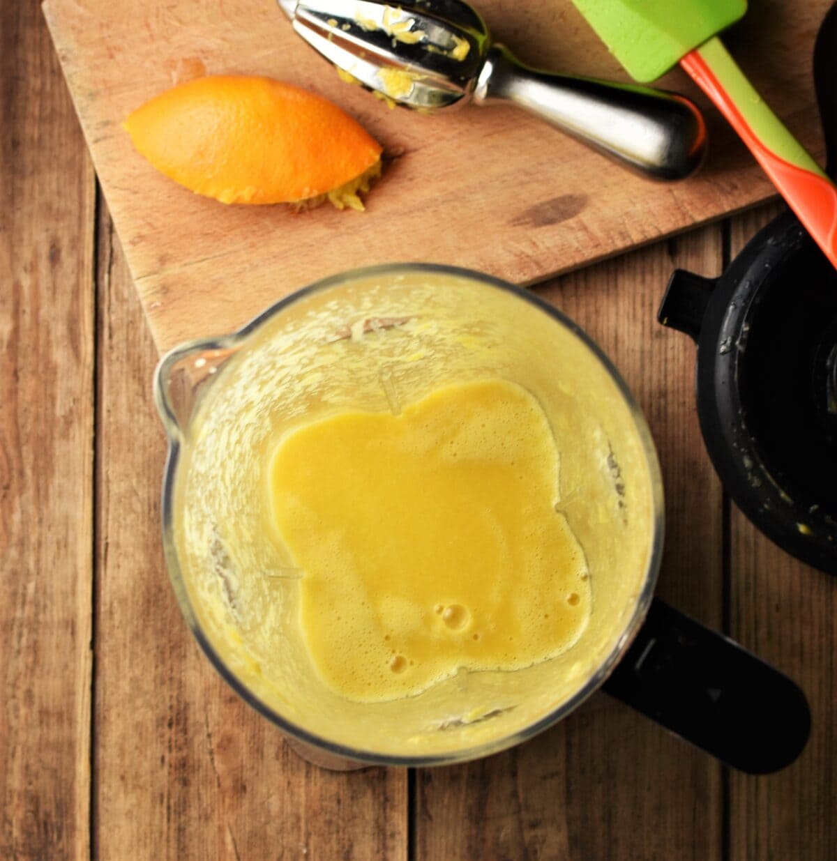 Orange sauce in blender, with orange peel, juicer and spatula on top of cutting board.