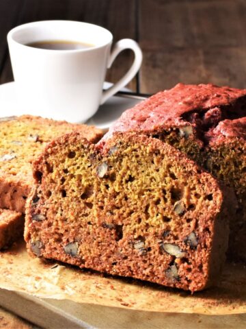 Side view of beetroot bread on top of parchment and cup of coffee in background.