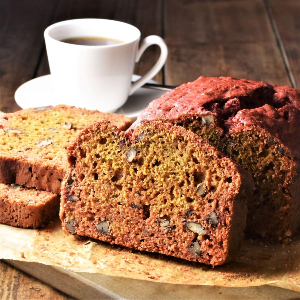 Side view of beetroot bread on top of parchment and cup of coffee in background.