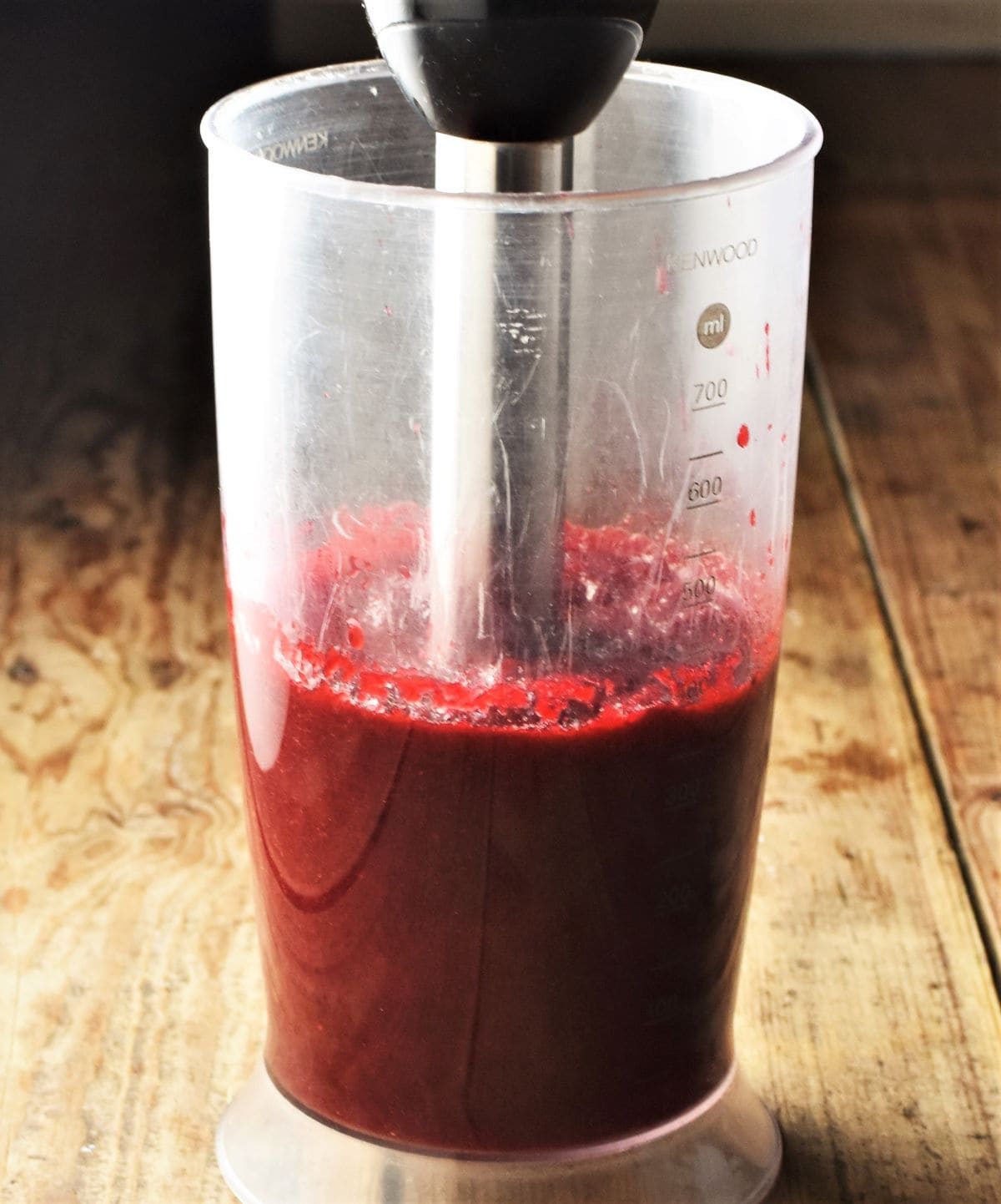Side view of beetroot mixture with blender stick in tall cup.