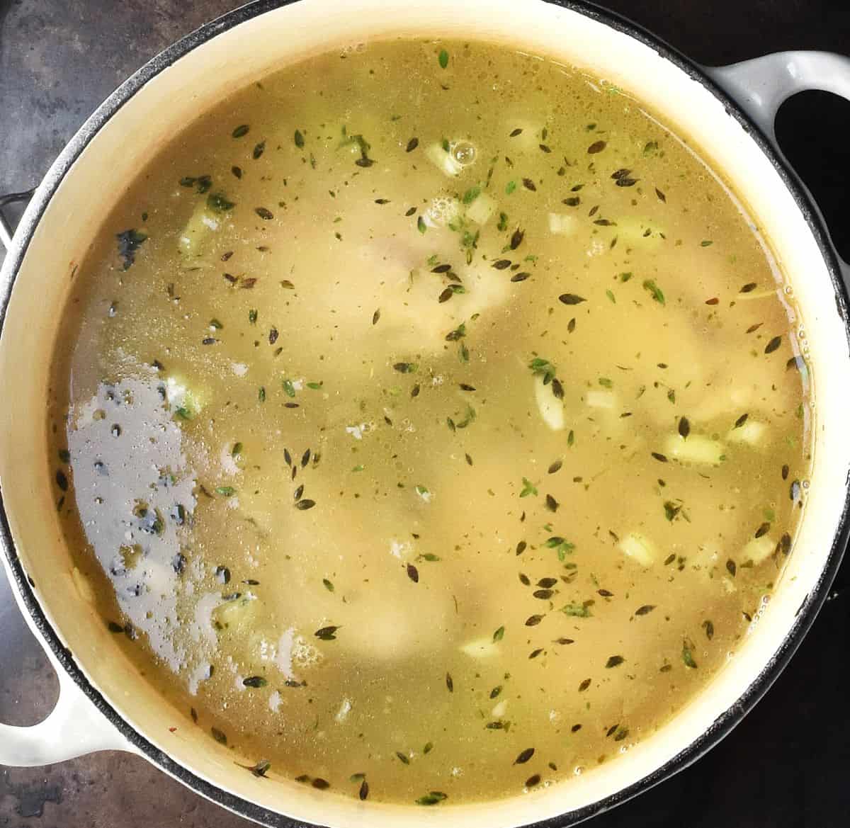 Skinless chicken thighs in broth in white pot.
