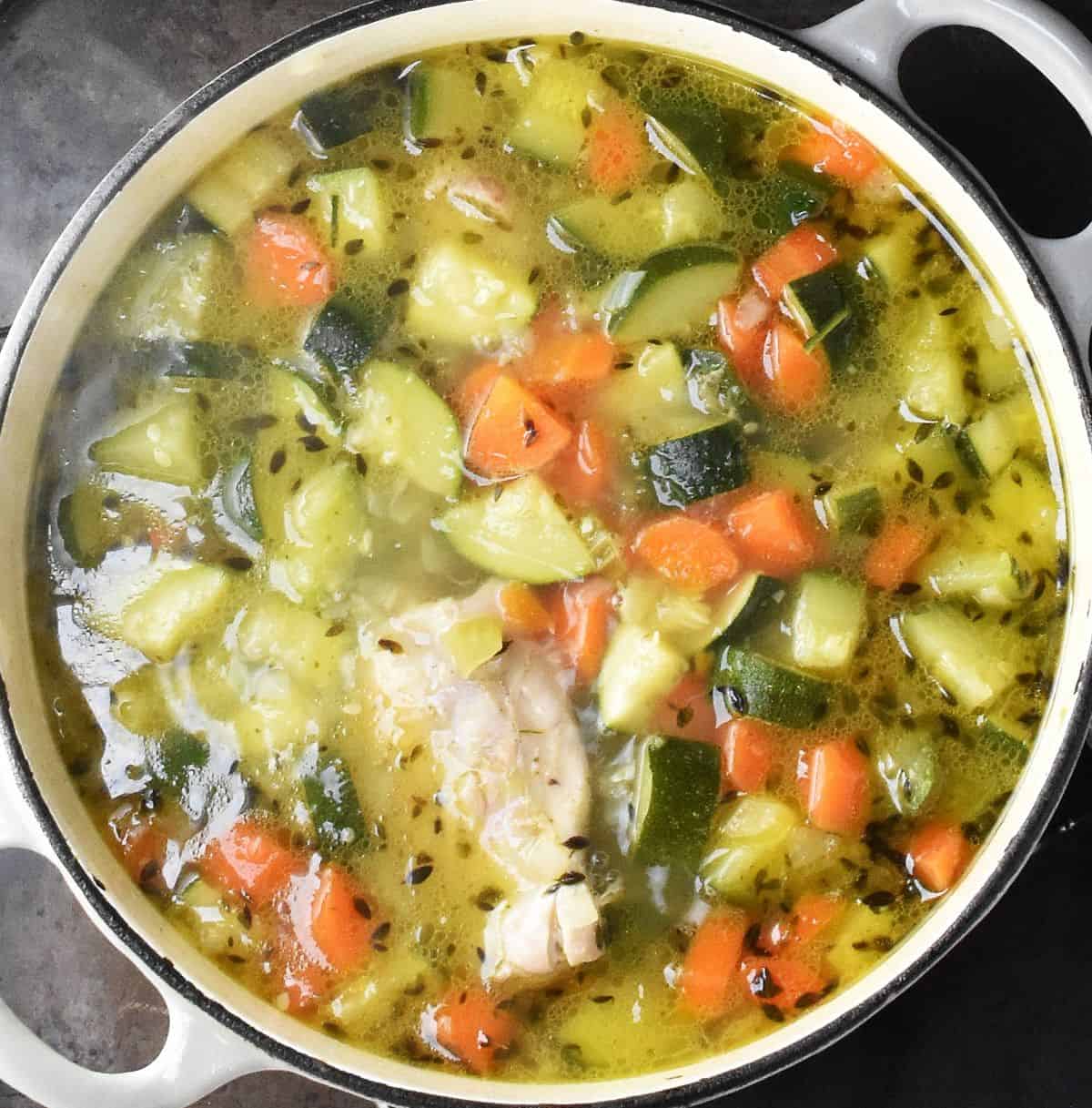 Diced zucchini and carrots in broth with chicken in white pot.