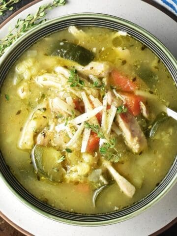 Top down view of chunky chicken zucchini soup in green bowl with spoon and thyme in background.