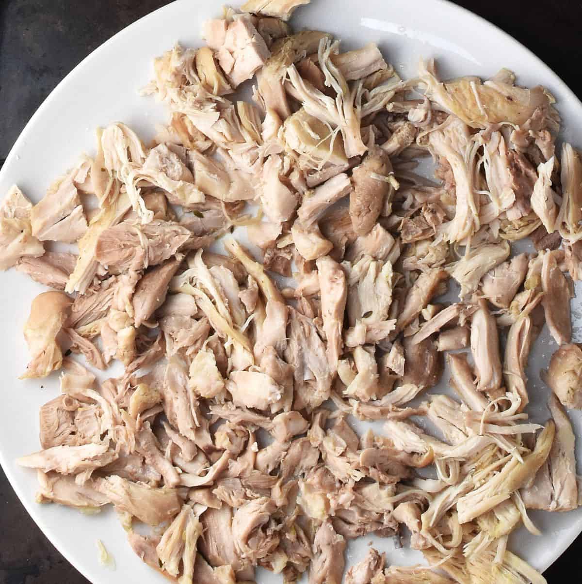 Chopped cooked chicken on white plate.