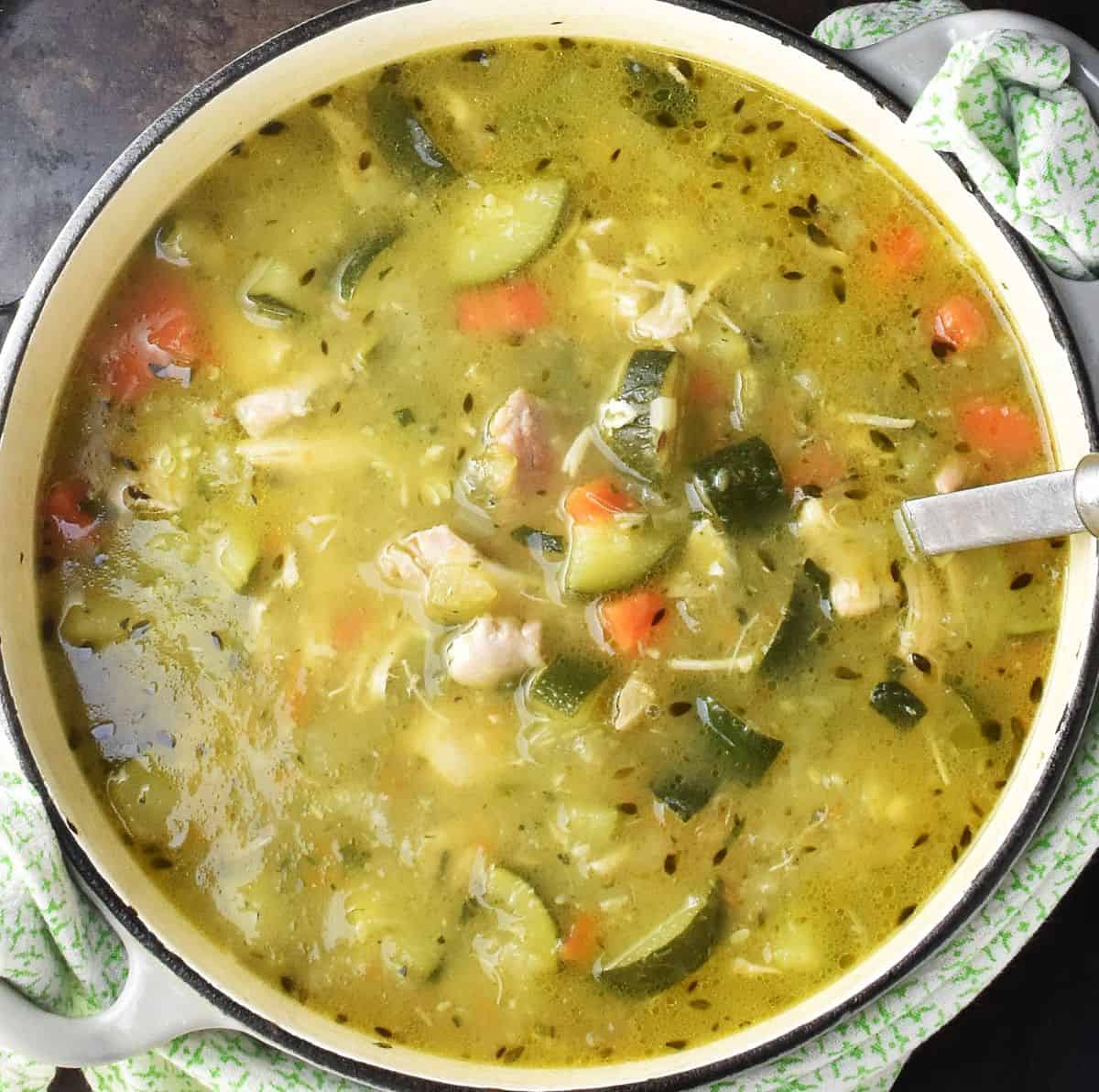 Chunky zucchini soup with chicken in white pot with ladle.