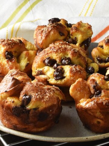 Side view of browned, baked french toast muffins on plate with cloth in background.