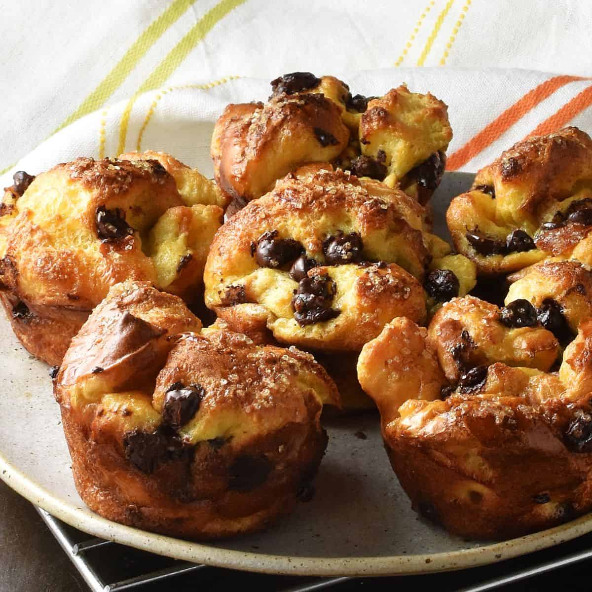 Side view of browned, baked french toast muffins on plate with cloth in background.
