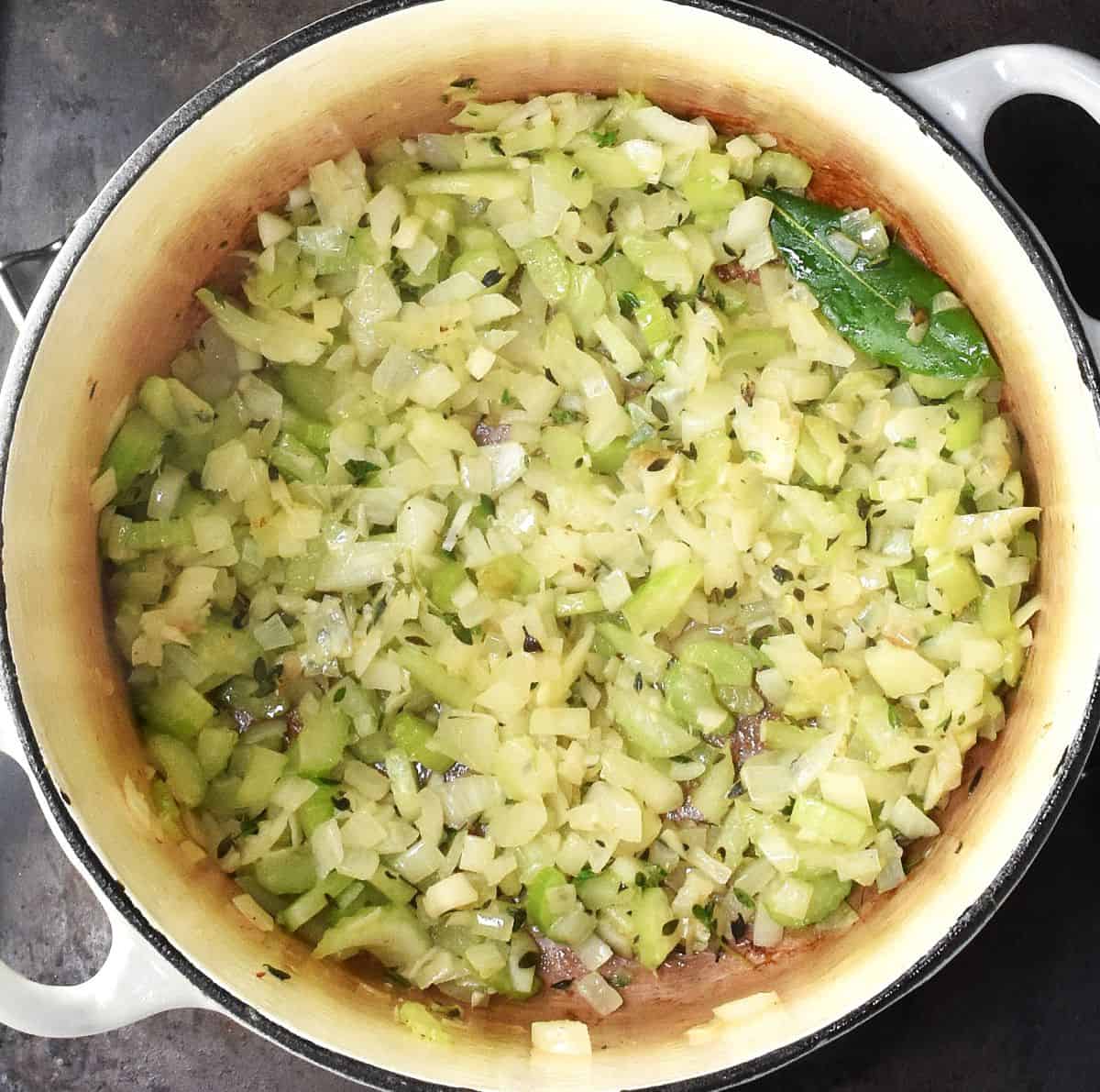 Diced onion and celery with bay leaf in white pot.