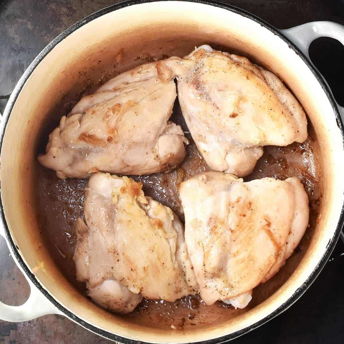 Top down view of 4 seared skinless chicken thighs in white pot.
