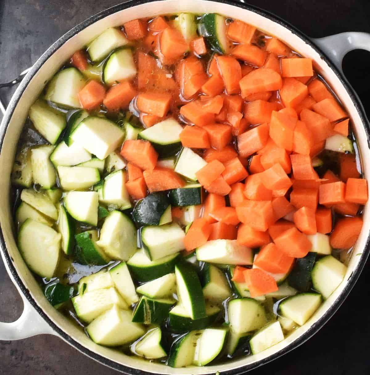 Top down view of diced carrots and zucchini in large, white pot.