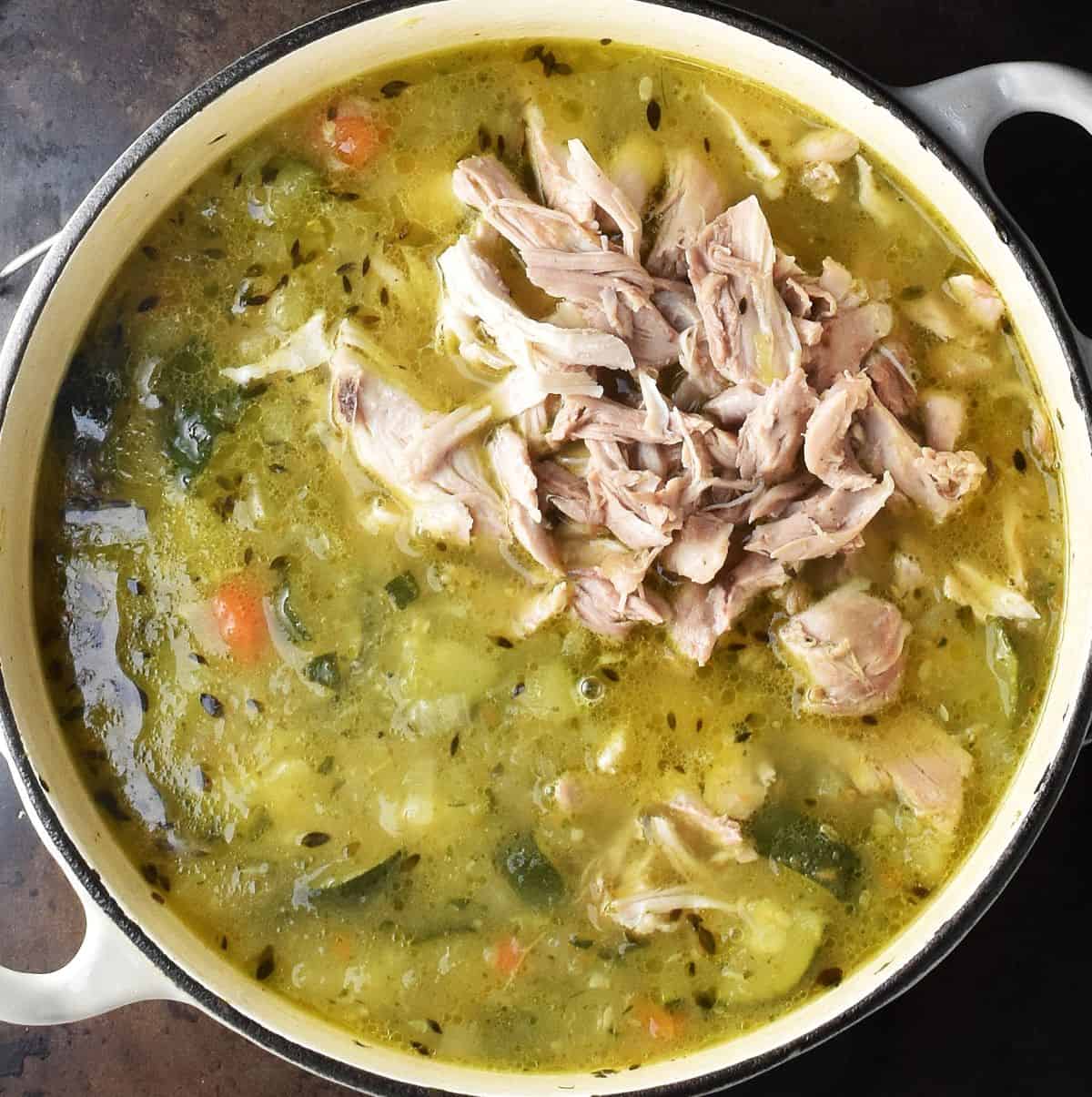 Top down view of chunky soup with zucchini and shredded chicken in white pot.