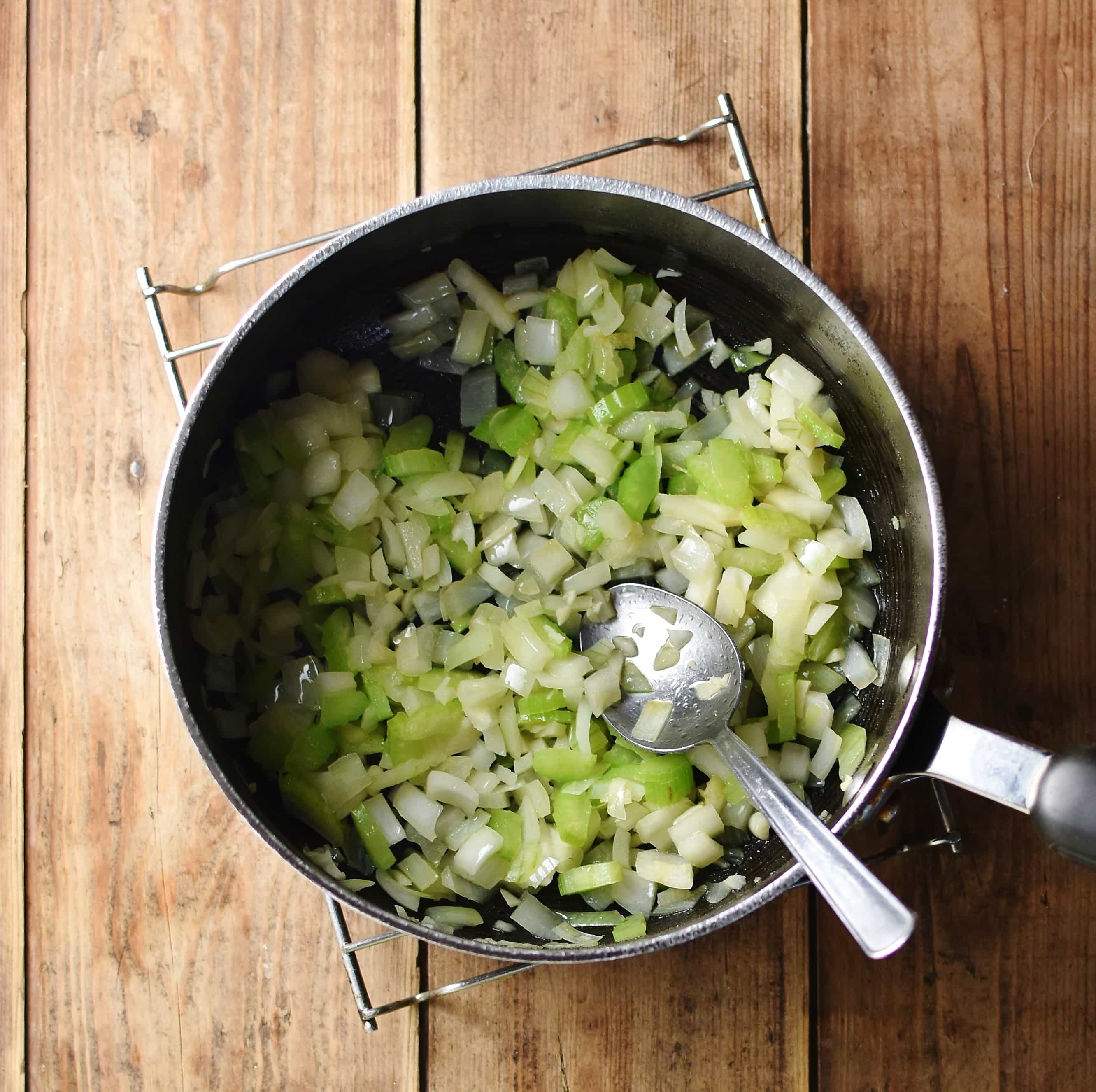 Chopped onions and celery in large pot with spoon.