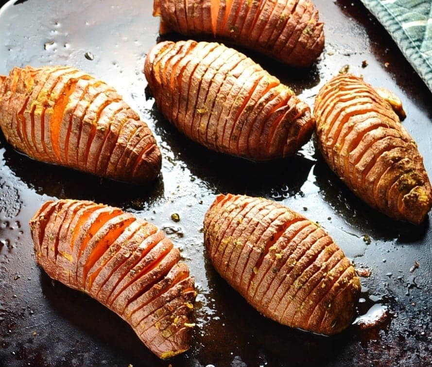 Close-up view of vegan Hasselback sweet potatoes on dark brown oven tray.