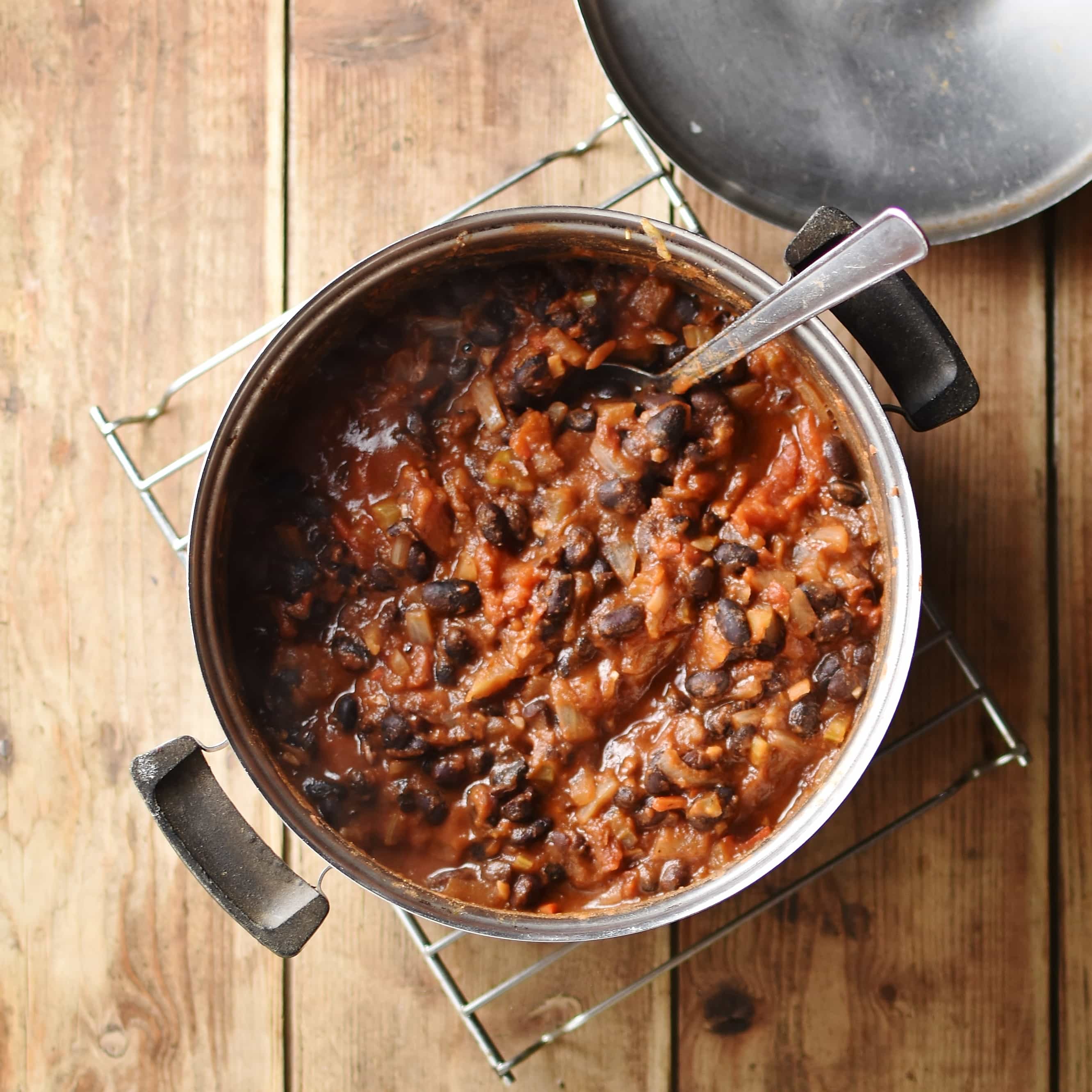 Top down view of black bean stew with spoon inside pot on top of cooling rack. 